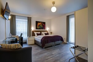 Una habitación de hotel moderna con cama, escritorio, silla, televisor y ventana con cortinas.