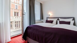 Una habitación de hotel con una cama grande, vistas a un edificio desde la ventana y un balcón.