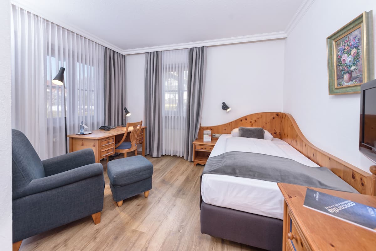 A hotel room with a bed, a desk, a chair, and a TV.