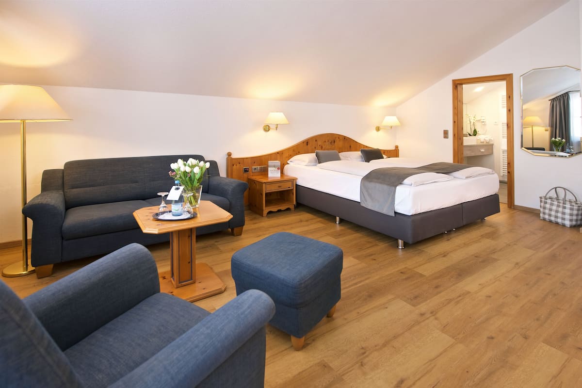 A modern, well-lit room with a sofa, a small table with a vase, a bed with a wooden headboard, and a mirror on the wall.