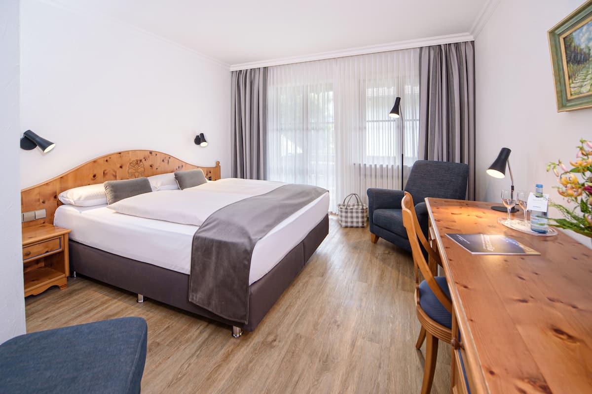 A hotel room with a wooden bed, a desk with a chair, a nightstand, and a lamp.