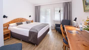 Quarto de hotel com cama de madeira, uma escrivaninha com cadeira, mesa de cabeceira e abajur.
