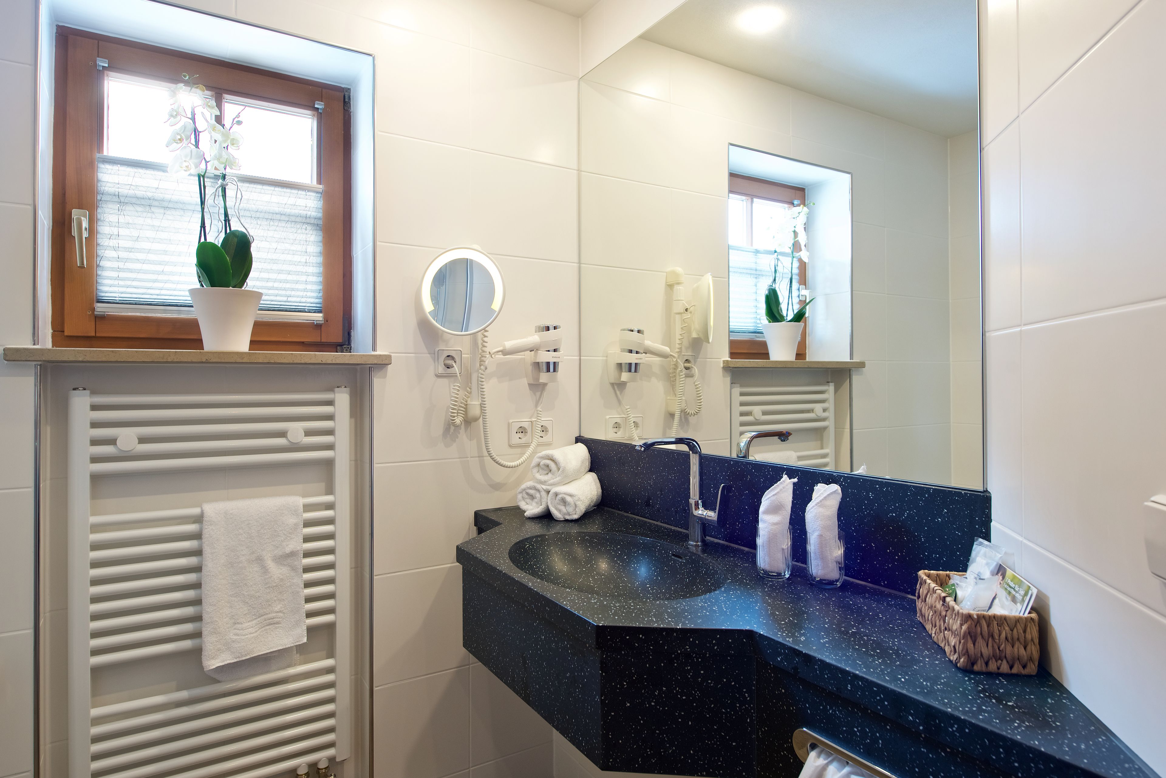 Un baño moderno con encimera negra, un perchero, un espejo y una planta en maceta.