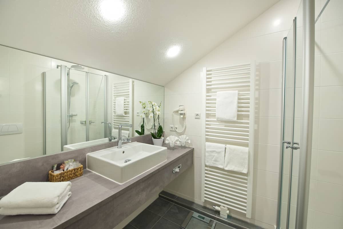 A modern bathroom with a large mirror, a sink, a shower, and a towel rack.