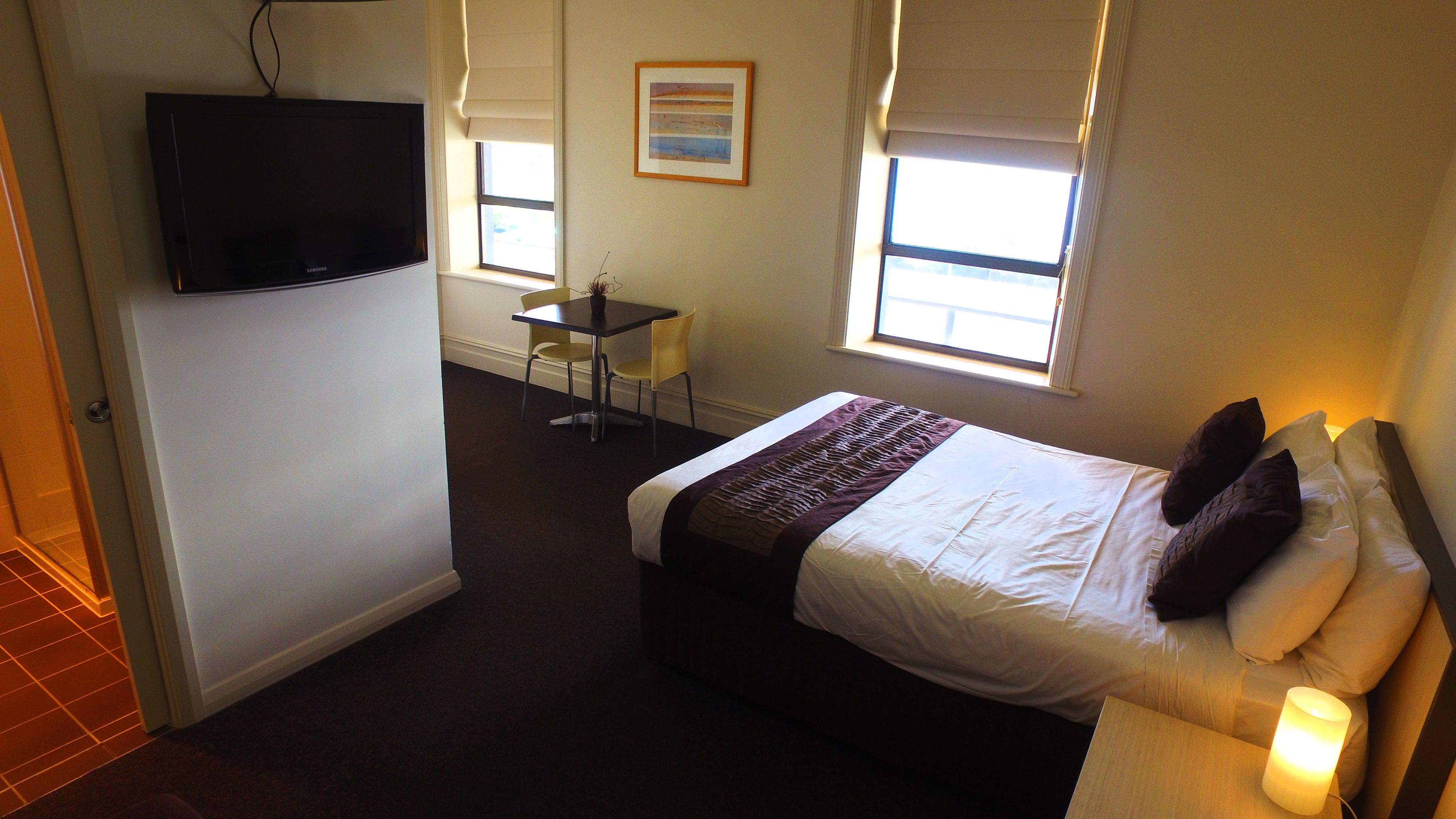 A hotel room with a bed, a TV, a desk, and two windows.