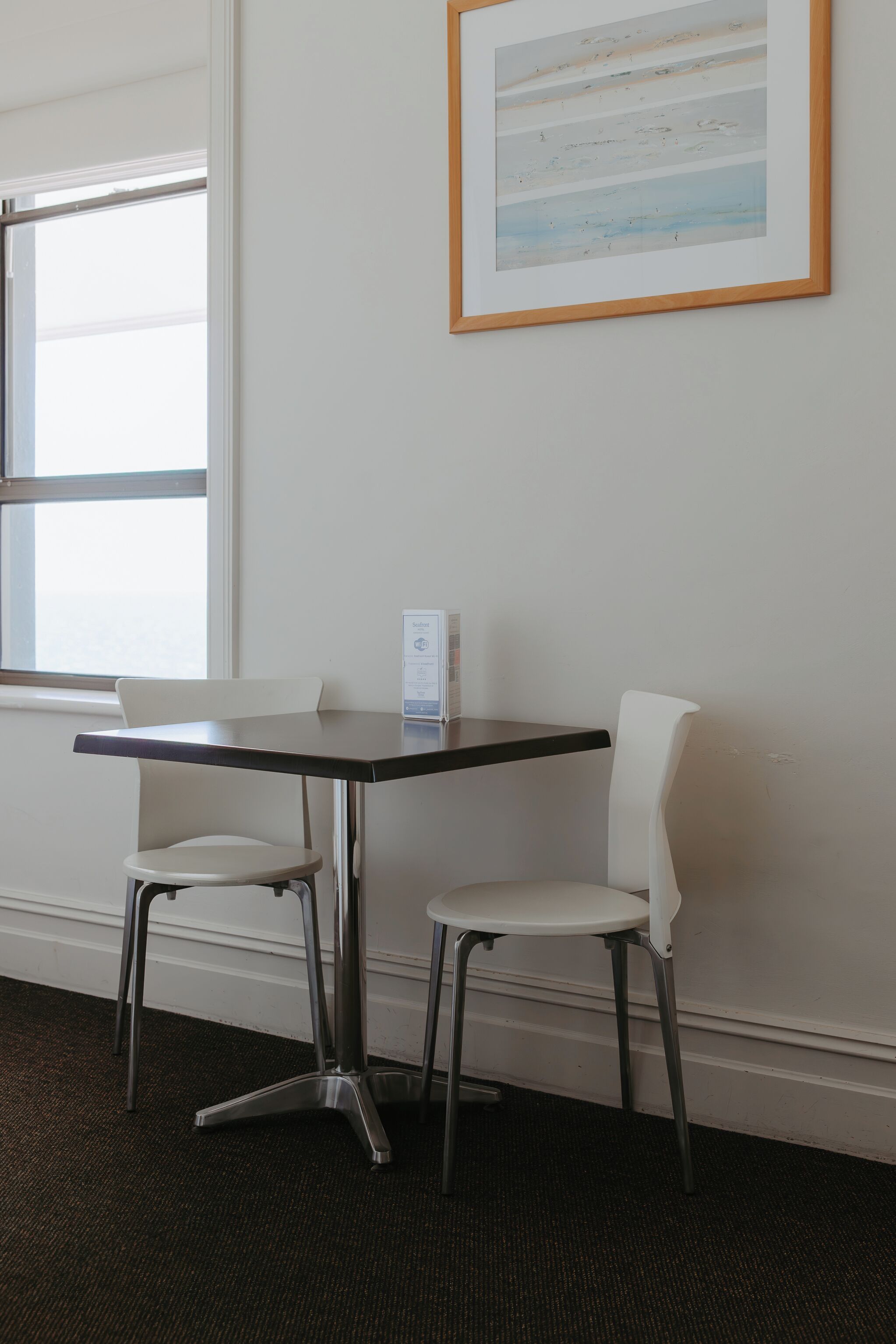 A small, modern room with a dark wooden table and two white chairs. A framed artwork hangs on the wall above the table.