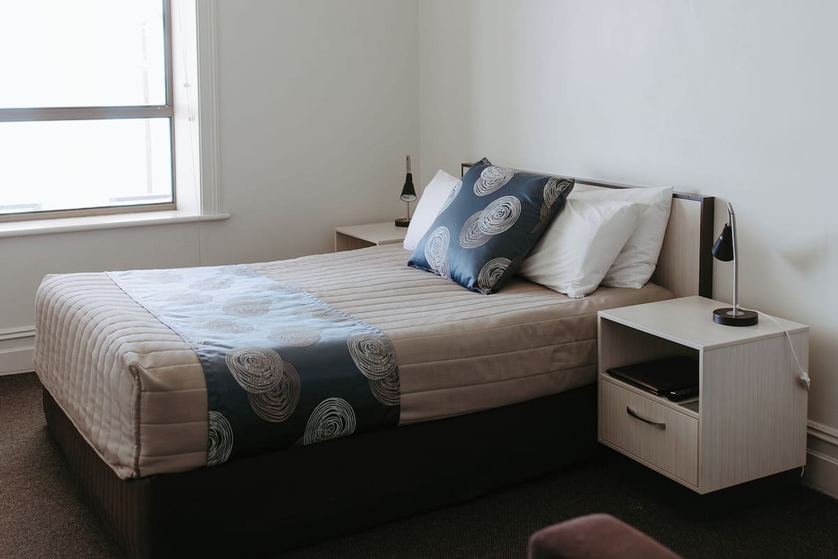 Une chambre à coucher comprenant un lit, des tables de chevet, une commode, une fenêtre et un luminaire fixé au mur.