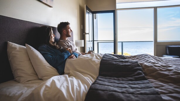 A hotel room with a large window, a bed with white and dark bedding, and a view of the sea. - Seafront Hotel Kangaroo Island (Penneshaw)