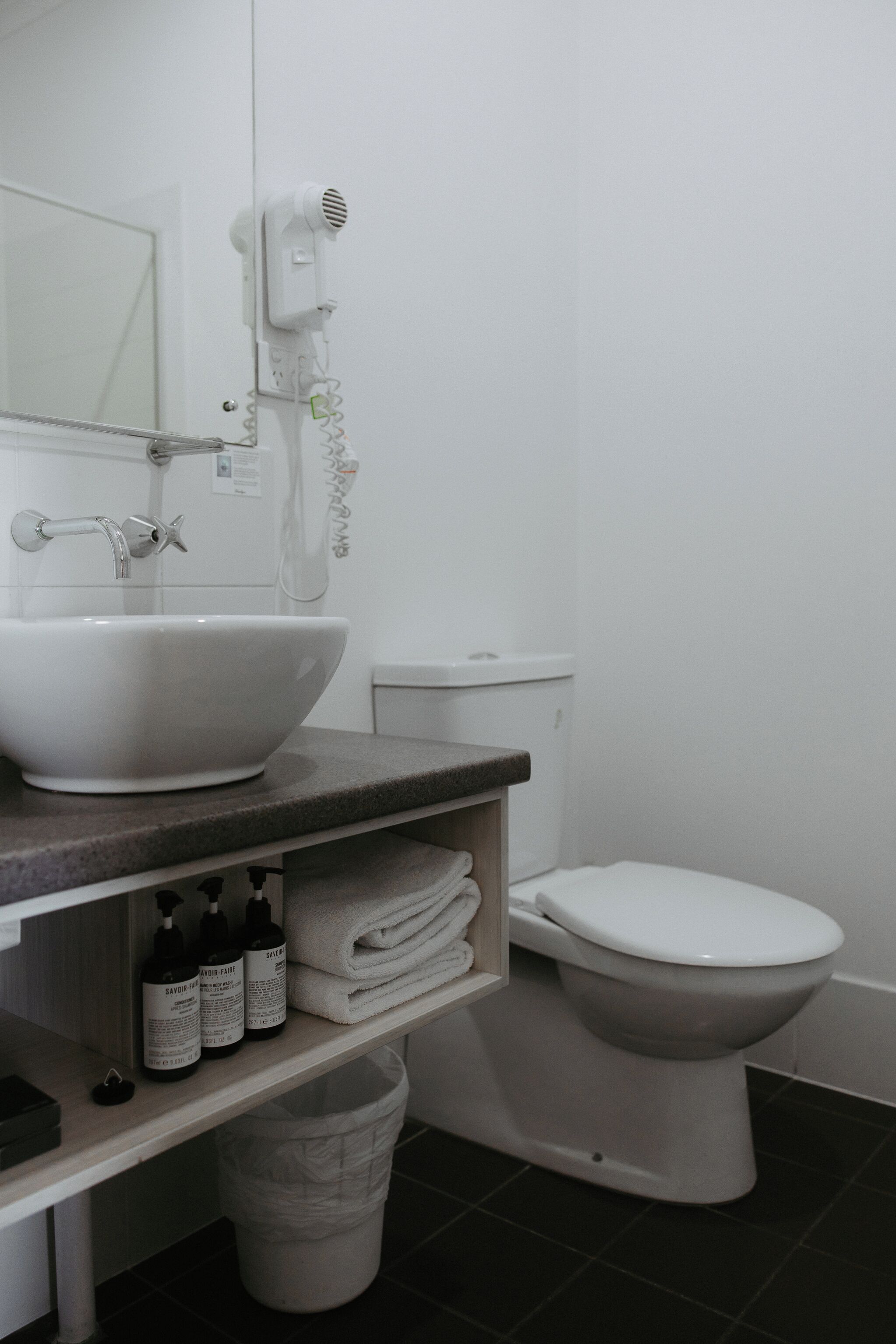 A bathroom with a white sink, a toilet, and a hairdryer mounted on the wall.