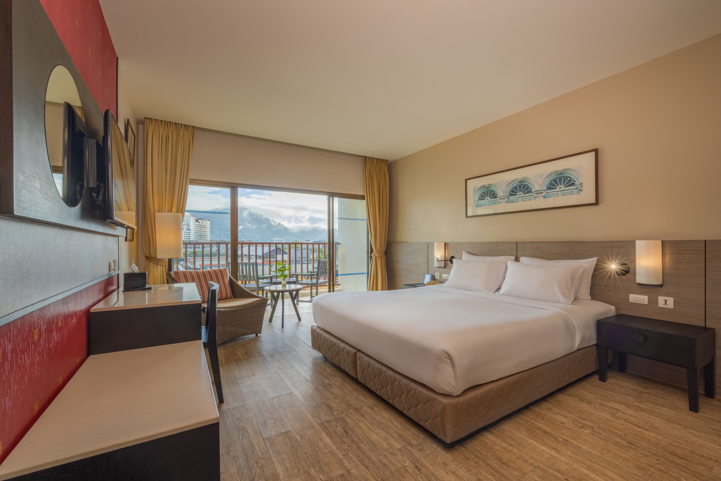 Habitación de hotel con una cama grande, un escritorio, una silla, una mesita con una planta y un balcón con vistas a montañas.