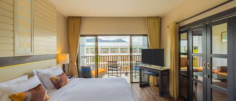 A hotel room with a large bed, a desk, a TV, and a balcony with a view of the sea.