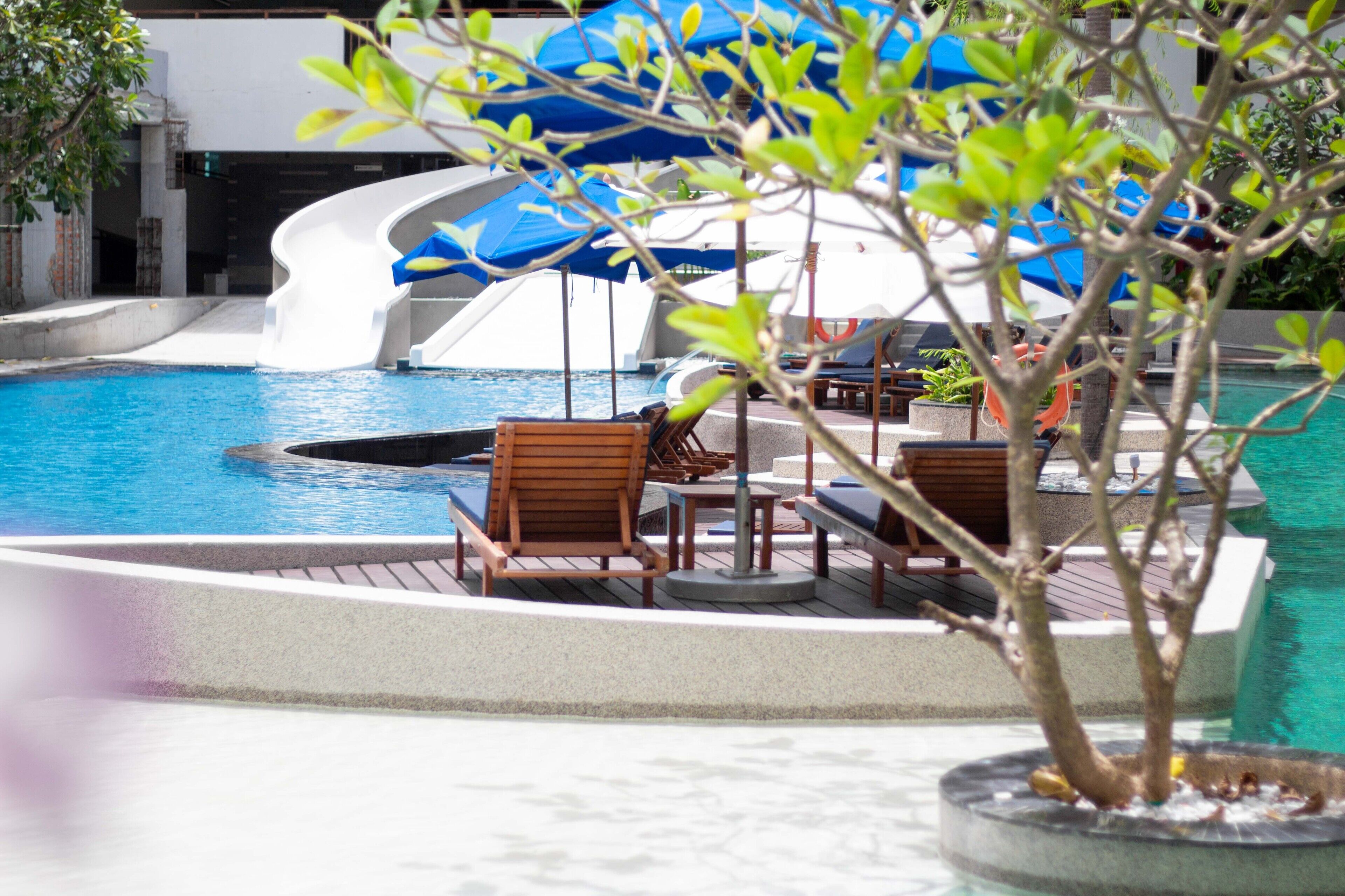 A pool area with a water slide, lounge chairs, and umbrellas.