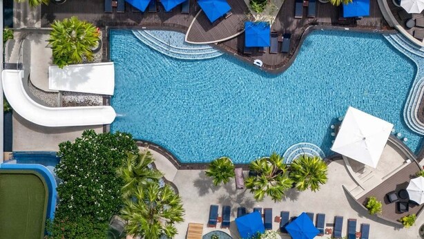 An aerial view of a resort with a central swimming pool, lounge areas with umbrellas, and surrounding greenery. - Deevana Plaza Phuket (Patong)