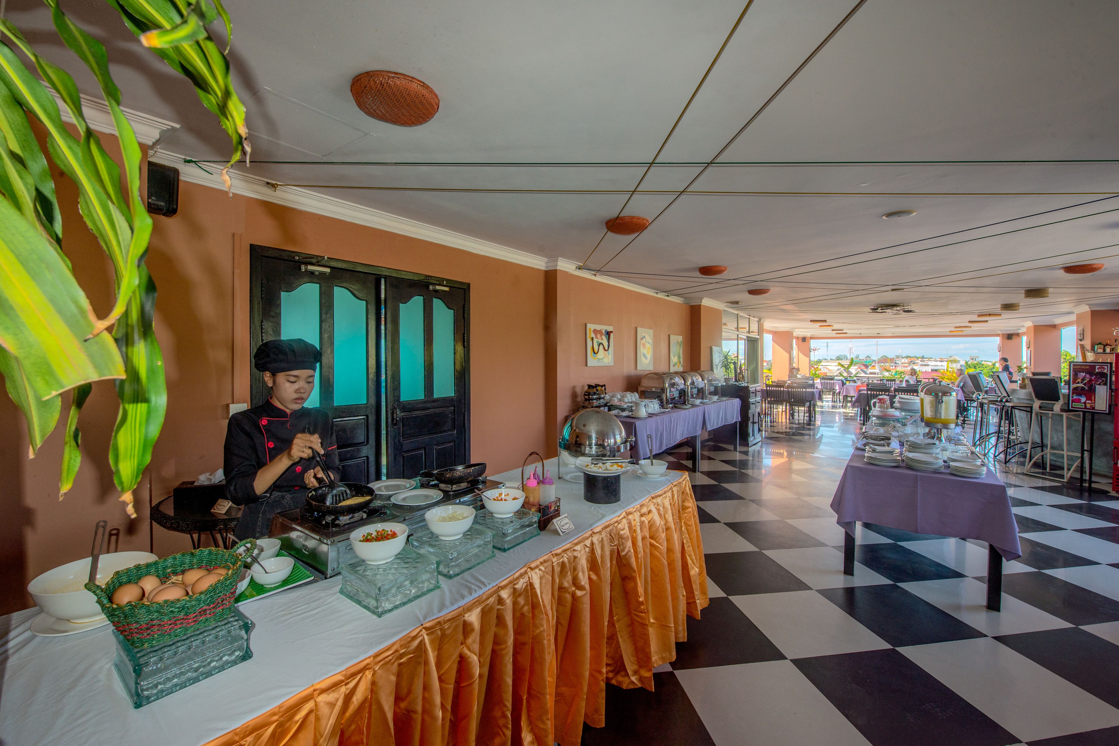 A buffet setup with a chef preparing food, a checkered floor, and a view of the outside.