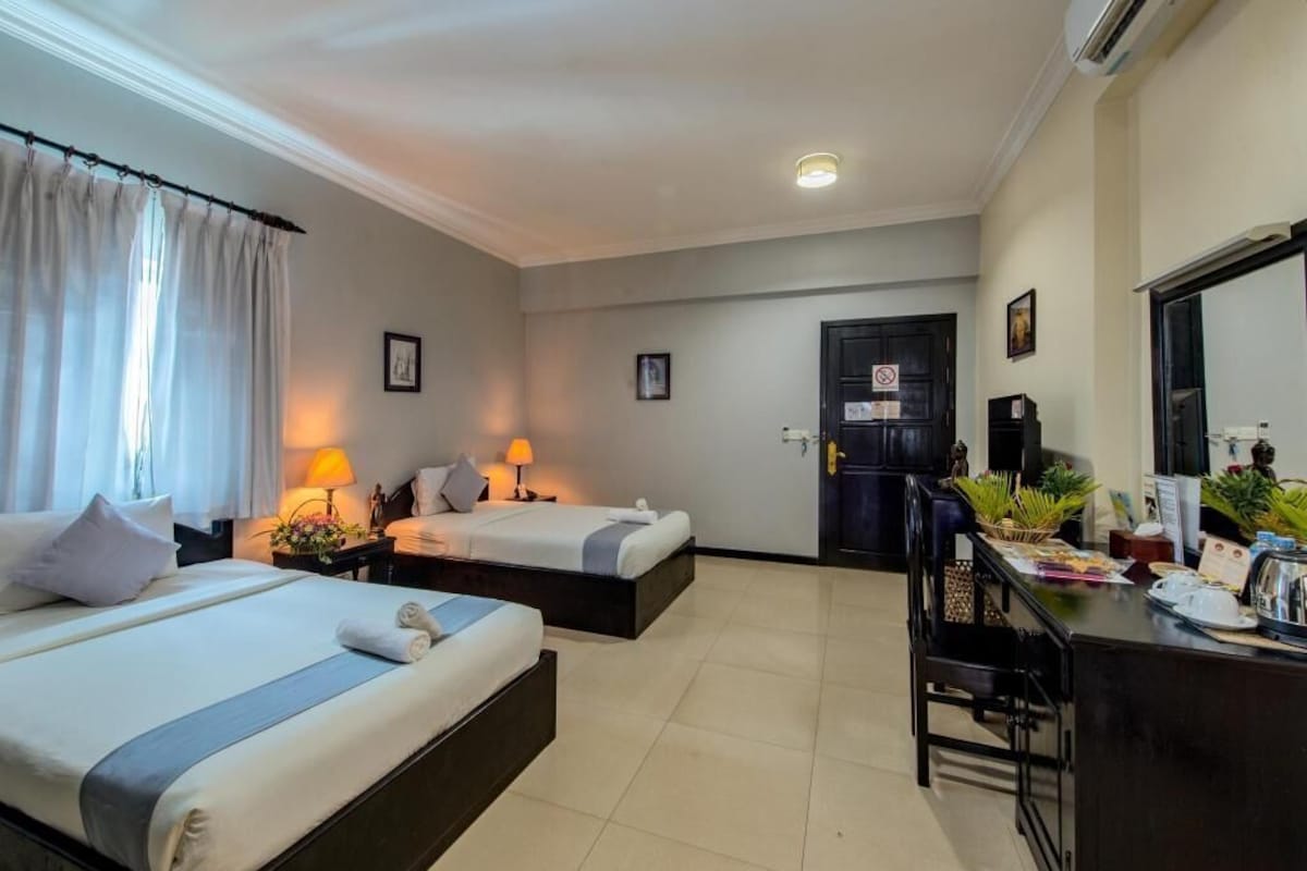 A hotel room with two beds, a desk, a chair, a door, and a small table with a plant.