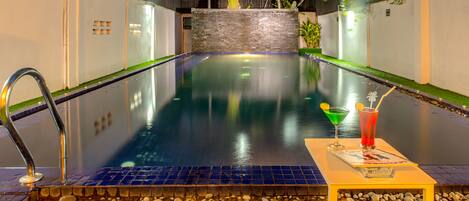 Una piscina interior tranquila con vistas despejadas a los edificios circundantes, una pared de piedra y una pequeña mesa con una bebida y un menú.