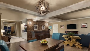 A modern living room with a dining table, blue chairs, a chandelier, a brick accent wall, and a television. - Hilton Columbia Center (Columbia)