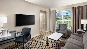 A hotel room with a large TV, a glass desk, a sofa, and a view of a building through the window. - Hilton Columbia Center (Columbia)
