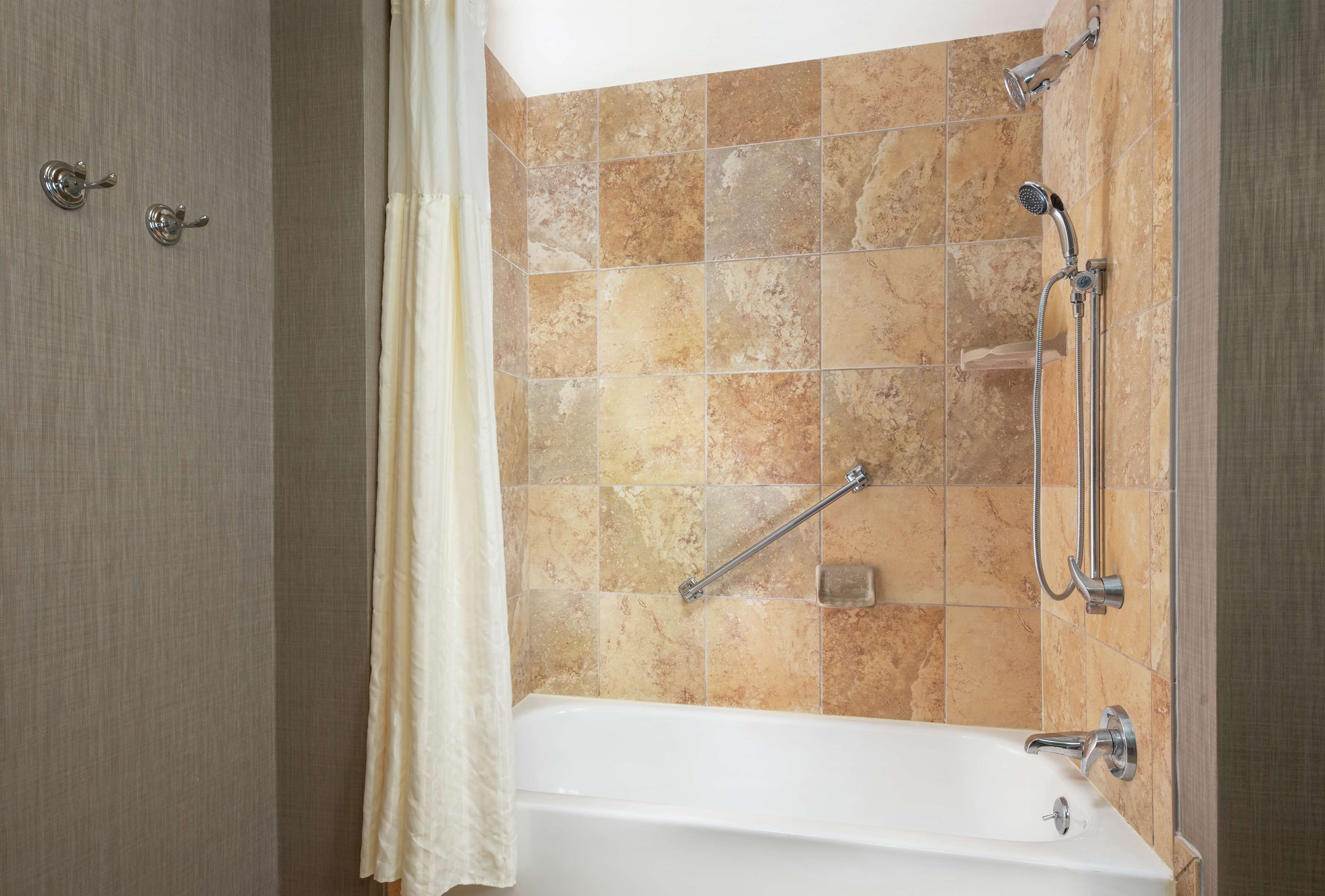 A bathroom with a bathtub, shower, and grab bars.