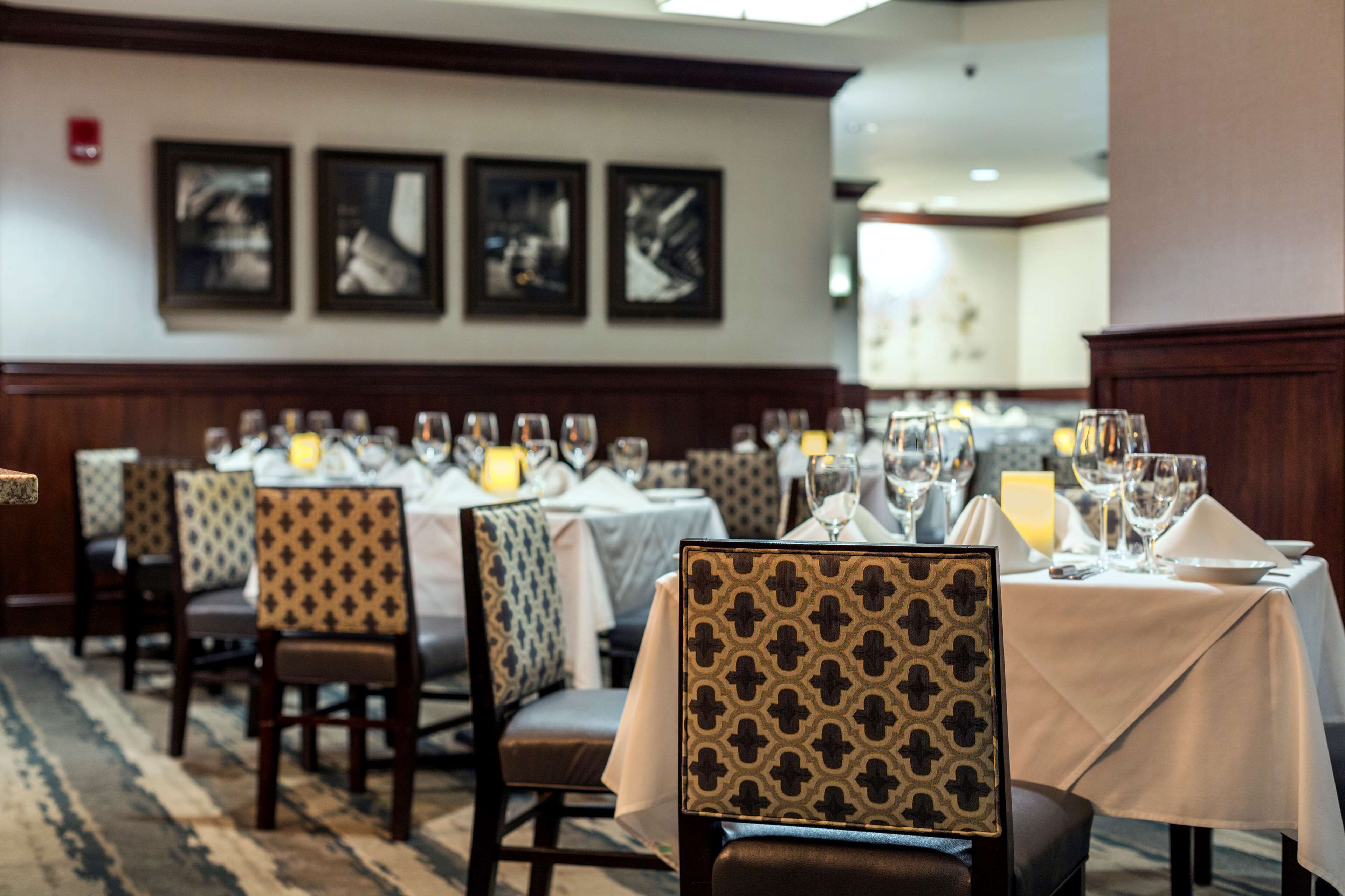 A dining area with tables set for service, chairs with patterned upholstery, and framed artwork on the wall.