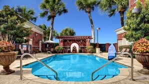 A swimming pool with a 3 FT no diving sign, surrounded by palm trees and a brick building.