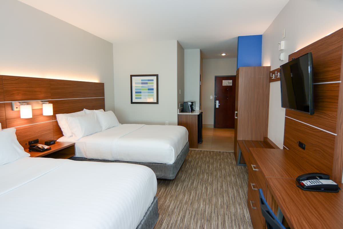 A hotel room with two beds, a desk with a telephone, a television, and a framed picture on the wall.