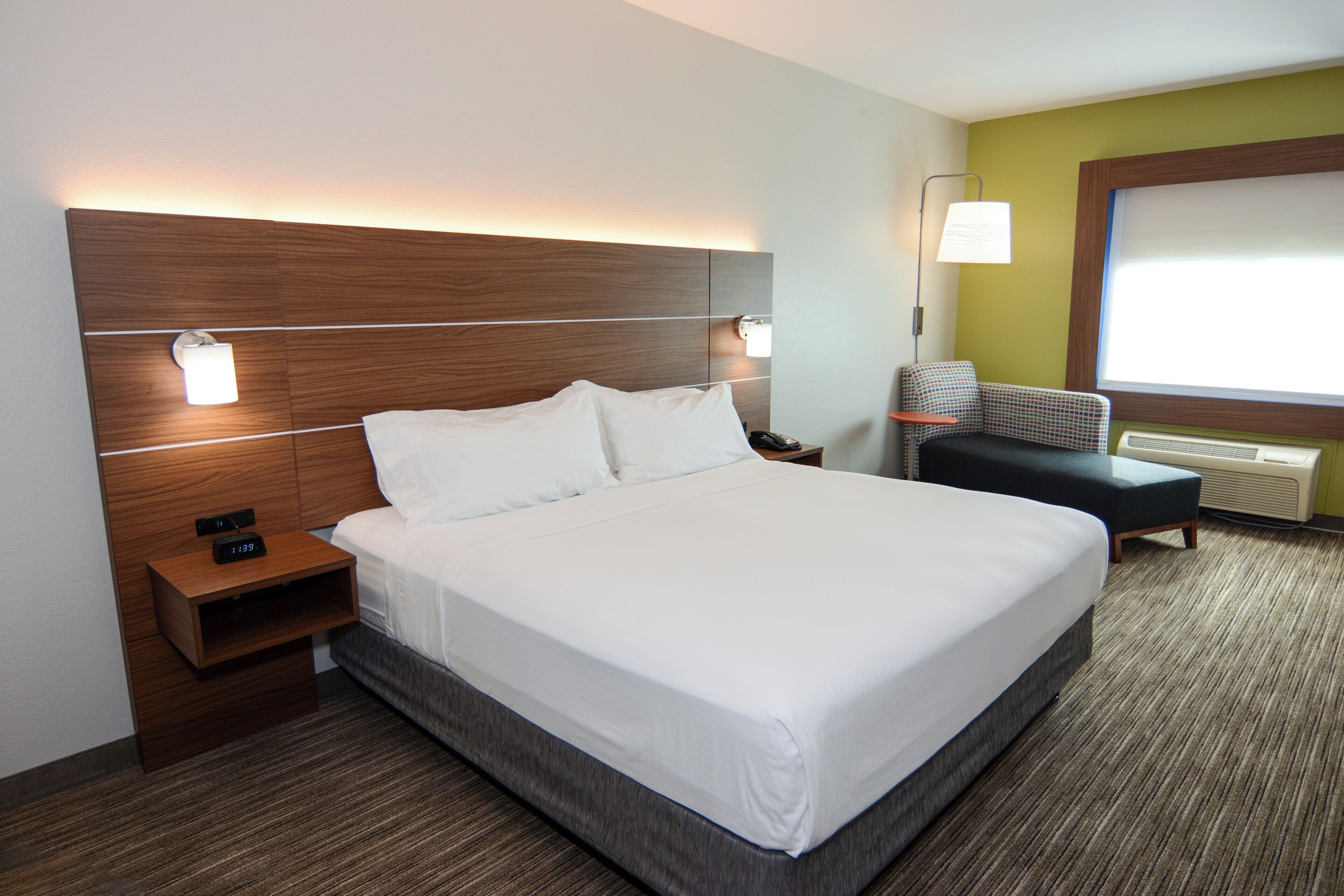 Ein Hotelzimmer mit einem großen Bett, Nachttischen, einem Sessel, einem Schreibtisch und einem Fenster.