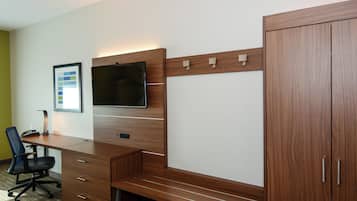 A hotel room with a wooden desk, a flat-screen TV, a chair, and a wardrobe.