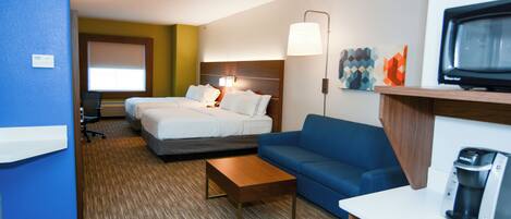 A hotel room with two beds, a sofa, a coffee machine, and a television.