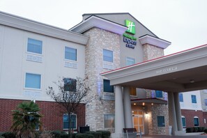 Ein Holiday Inn Express & Suites Hotel mit Steinfassade, zahlreichen Fenstern und einem überdachten Eingangsbereich.