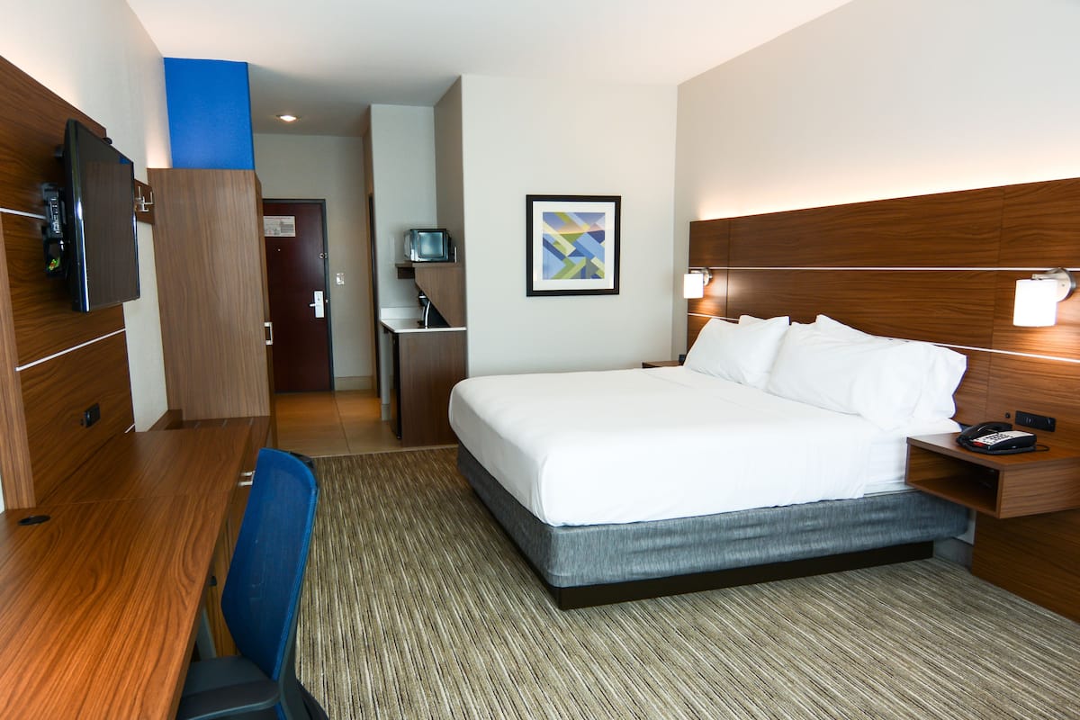 A hotel room with a bed, desk, chair, TV, and a framed picture on the wall.
