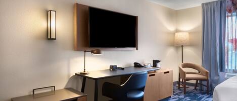 Una habitación de hotel con escritorio, silla, televisión de pantalla plana, lámpara y cama.