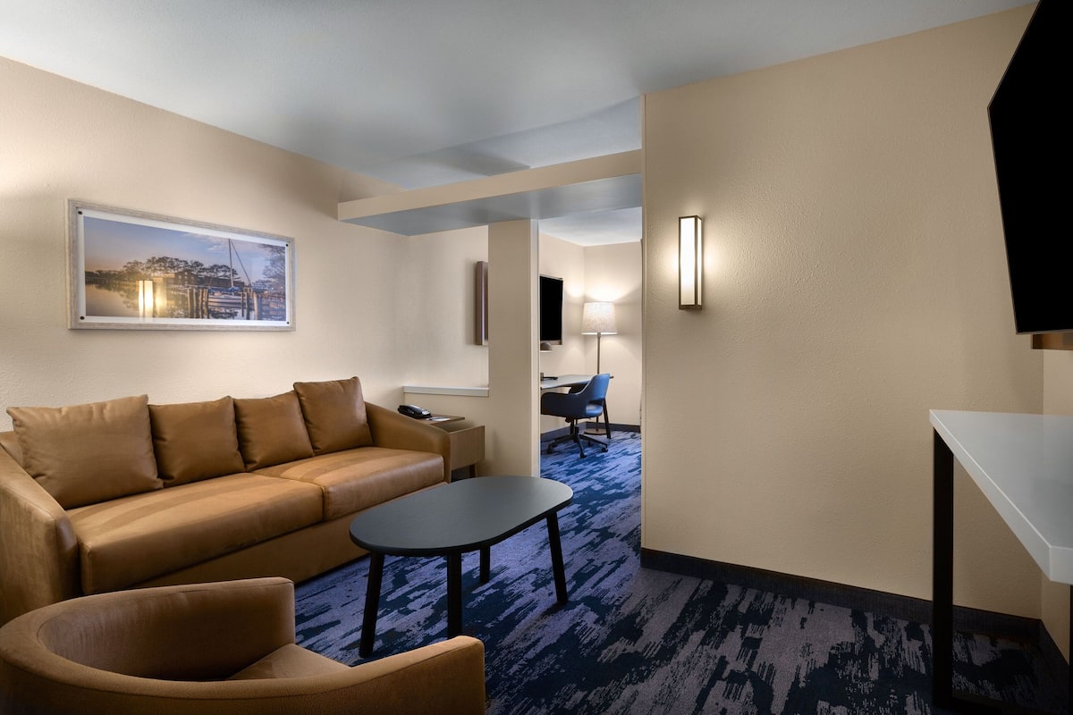 A hotel room with a beige sofa, a small round table, a blue patterned carpet, and a framed picture on the wall.