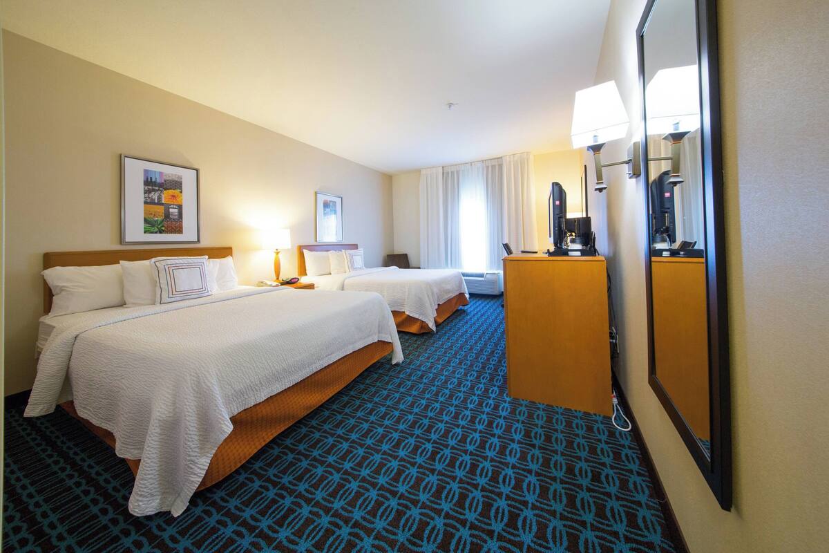 A hotel room with two beds, a desk, a mirror, and a patterned carpet.