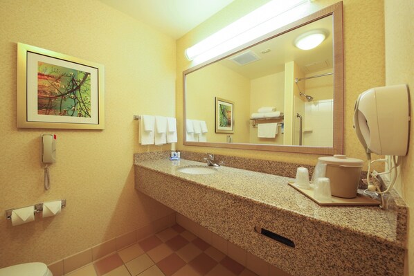 A hotel bathroom with a granite countertop, a large mirror, a hairdryer, and a telephone.