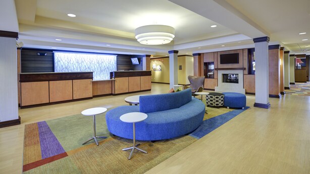 A modern lobby with a curved blue seating area, a reception desk, and a television screen. - Fairfield Inn & Suites by Marriott Cordele (Cordele)