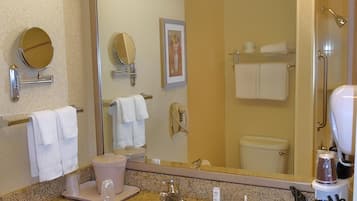 A hotel bathroom with a sink, mirror, towel rack, toilet, and shower area.