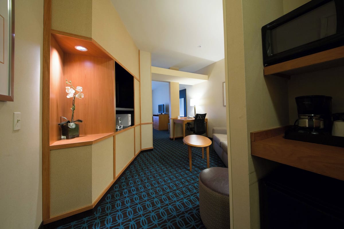 A hotel room with a kitchenette, a small seating area, and a desk.