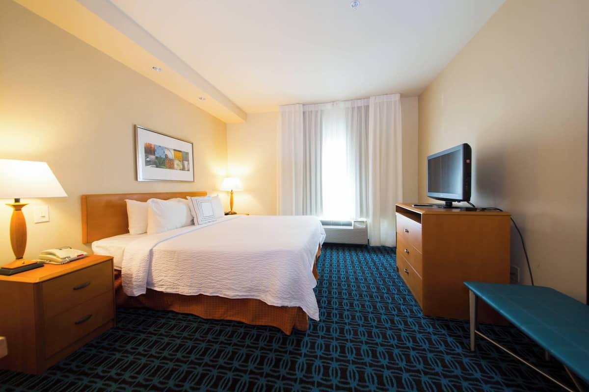 A hotel room with a bed, bedside lamps, a television on a wooden dresser, and a patterned carpet.