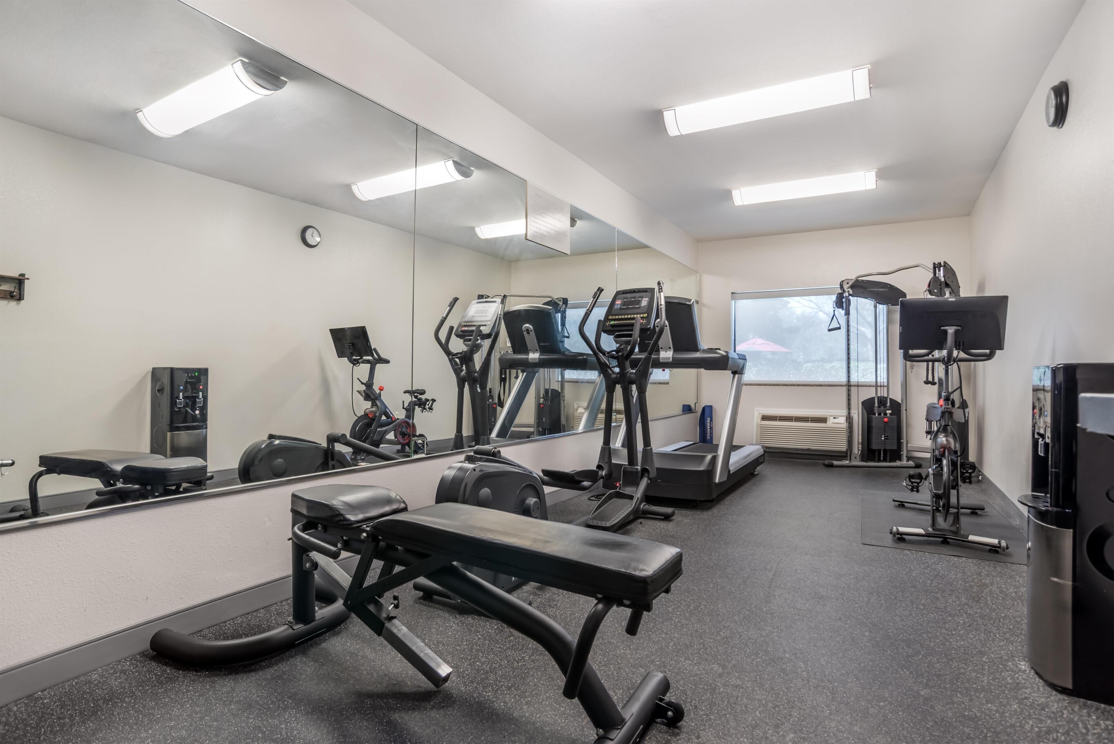 Ein Fitnessraum mit Trainingsgeräten, einer Bank und einem großen Spiegel.
