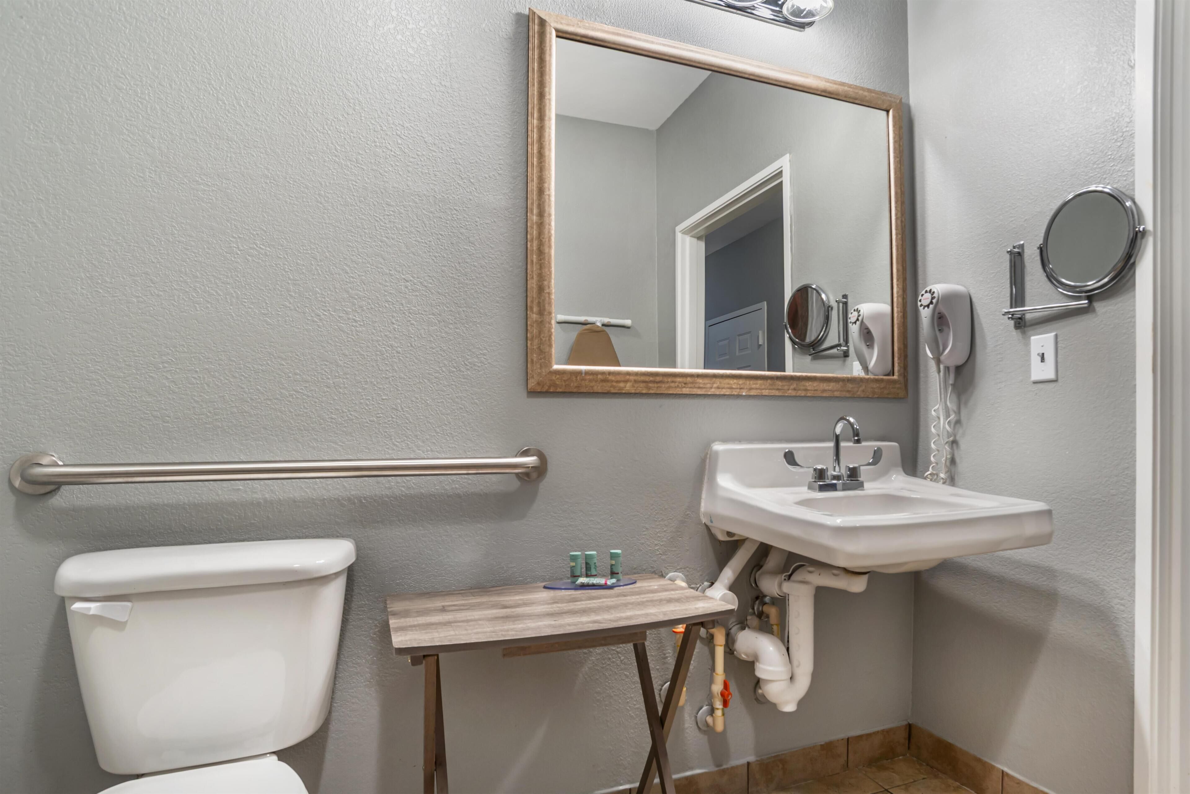 A bathroom with a toilet, sink, mirror, and hand dryer.