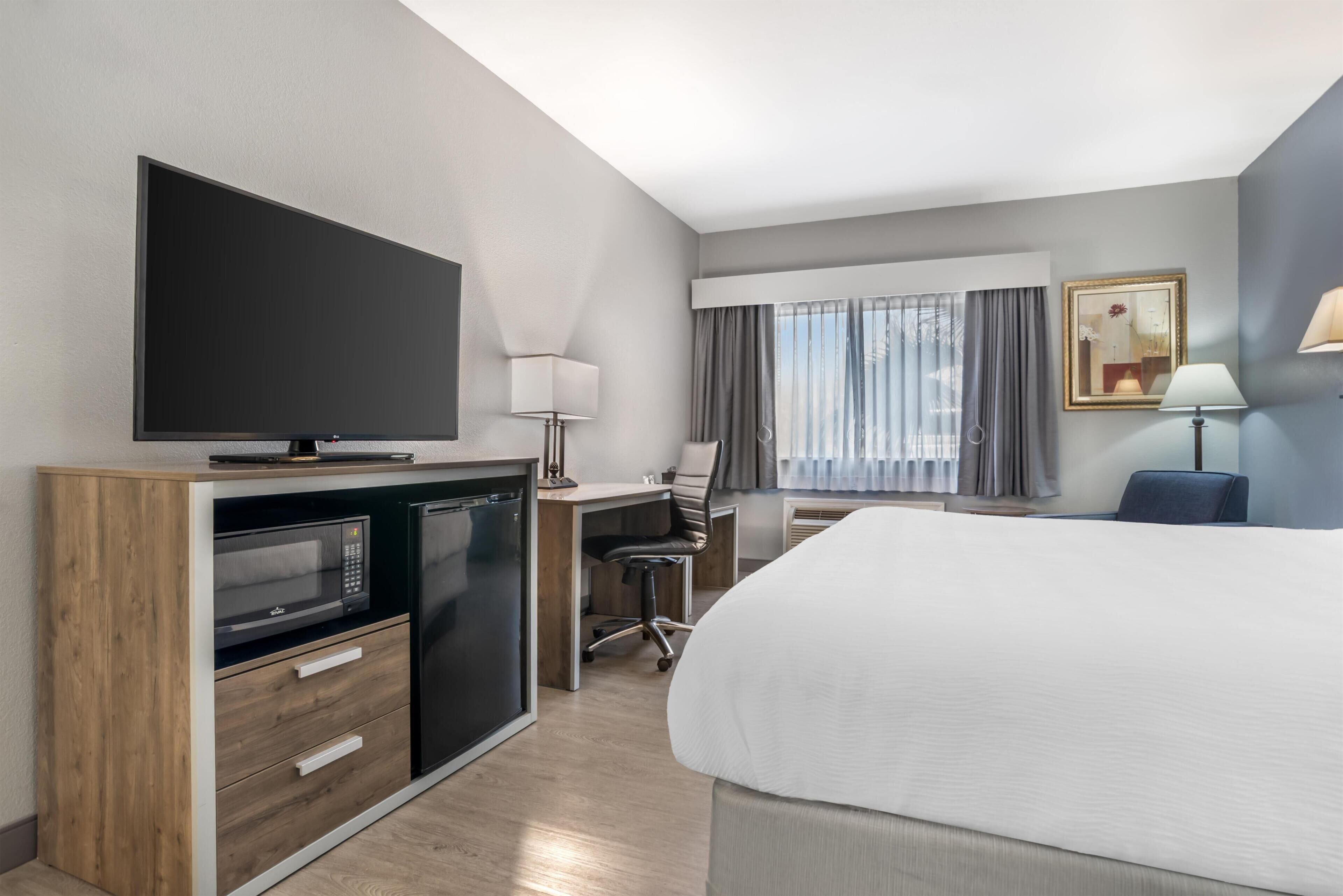 Ein Hotelzimmer mit Bett, Schreibtisch mit Stuhl, Fernseher, Mikrowelle und Kühlschrank.