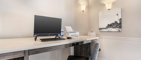 Una habitación de hotel moderna con escritorio, computadora, impresora y un cuadro de un faro.