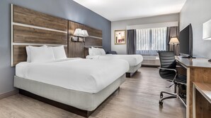 Ein Hotelzimmer mit zwei Betten, einem Schreibtisch, einem Sessel, einem Fernseher und einem Fenster mit Vorhängen.
