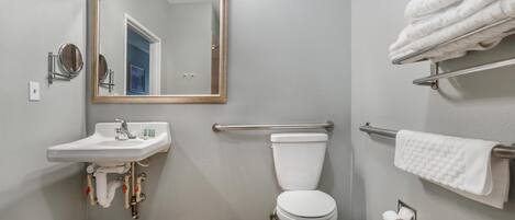 Un baño con lavamanos, espejo, inodoro, toallero y barras de apoyo.