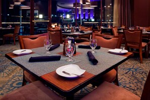 Um restaurante com mesas postas para refeições, cadeiras e vista para a paisagem urbana.