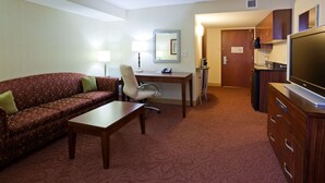 A hotel room with a sofa, desk, chair, television, and a kitchenette area.