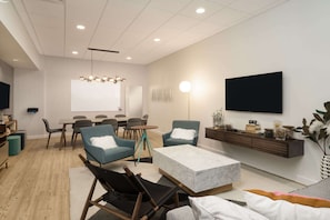 A modern living room with a flat-screen TV, a dining area, and a seating area with sofas and chairs.