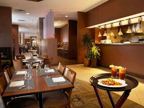 Restaurante com mesas preparadas para refeições, área de bar e uma planta decorativa.
