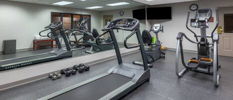 Une salle de sport équipée de tapis de course, d’haltères et d’un mur recouvert de miroirs.